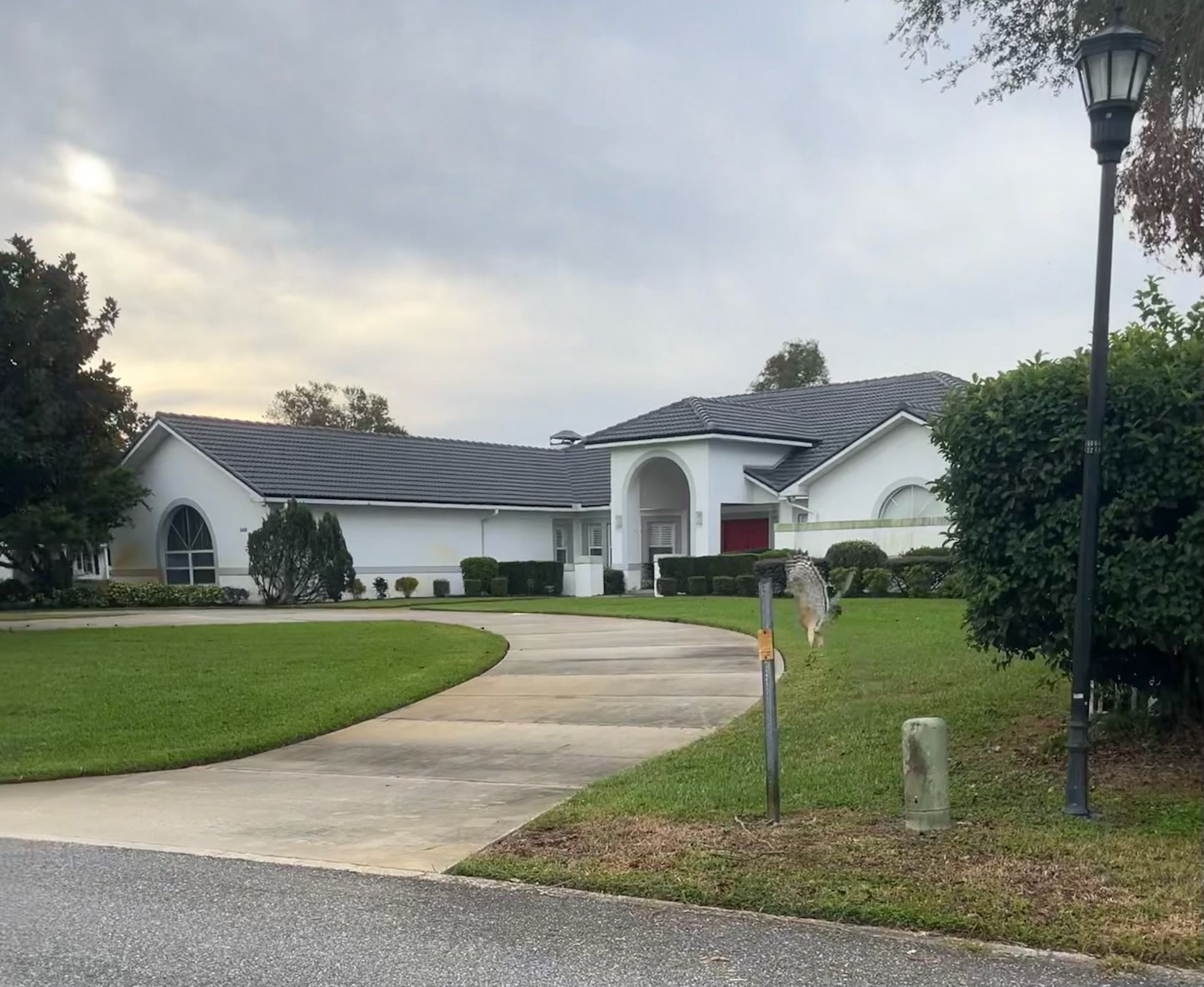 White house with dark roof and curved driveway on a cloudy day.