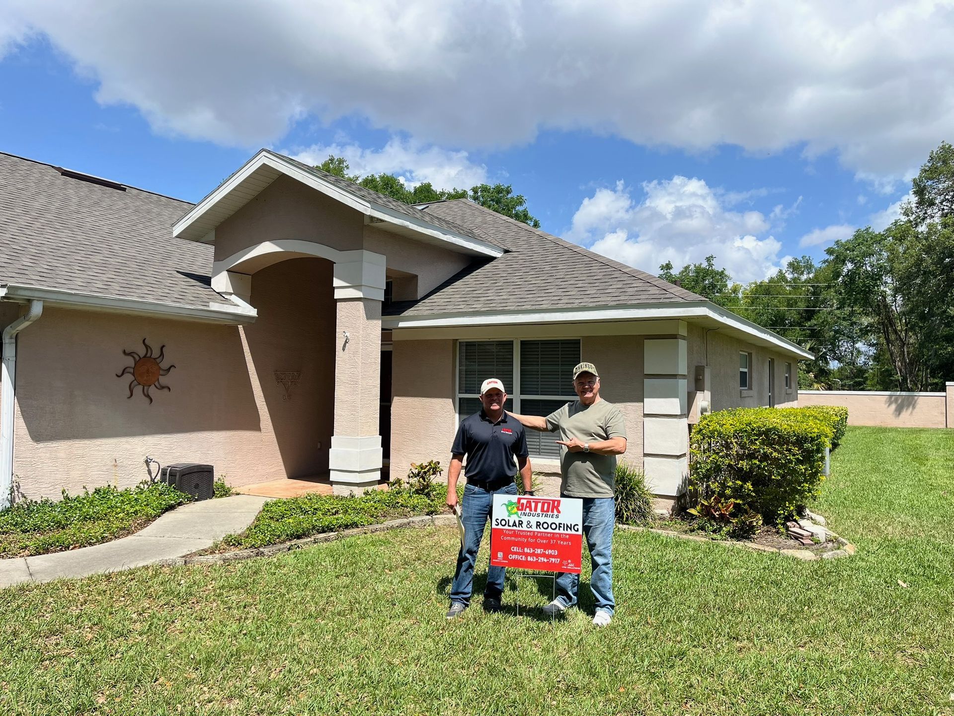 Two men in front of a house, holding a 