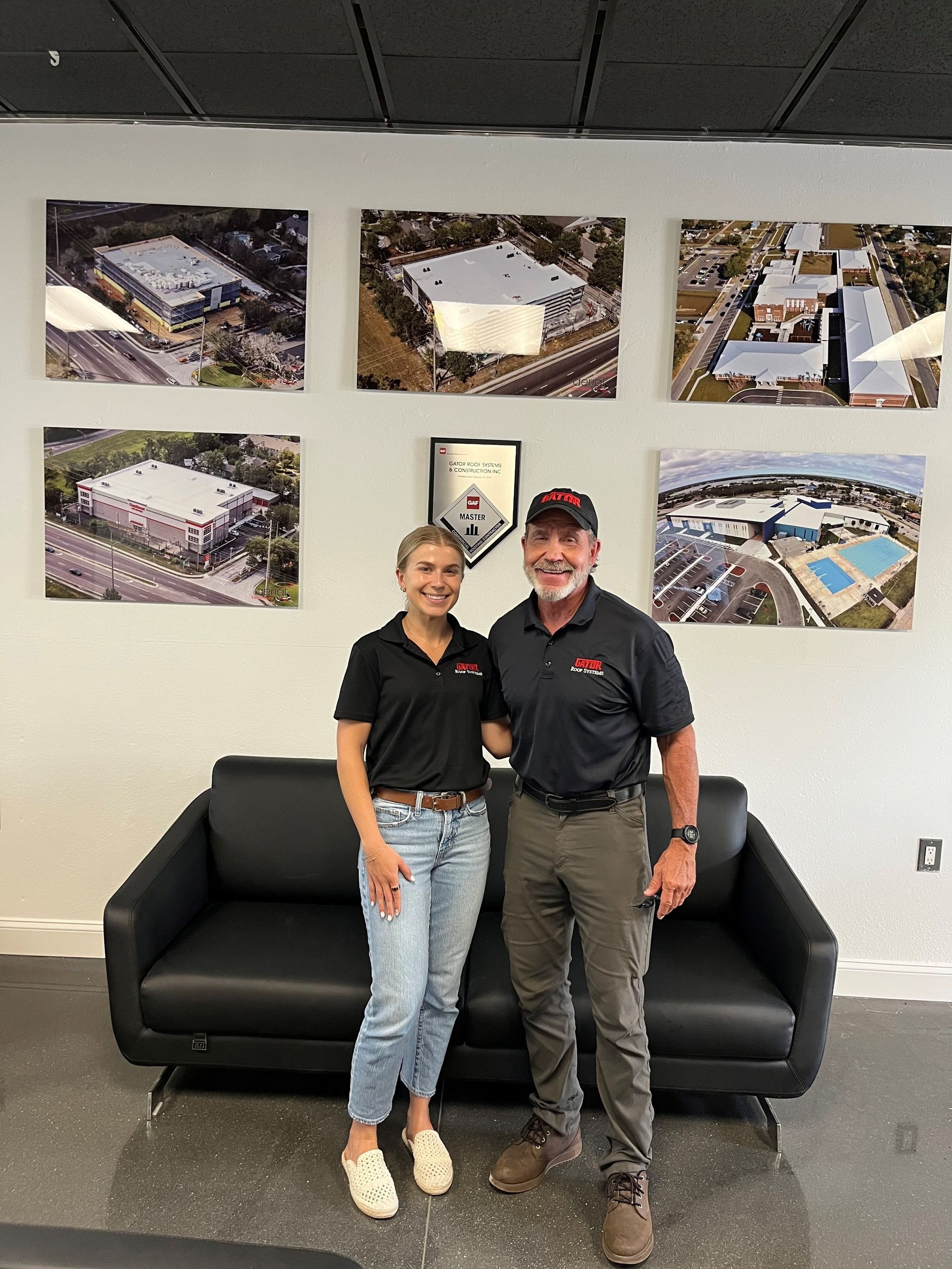Two people standing in an office lobby in front of a black couch and wall photos.