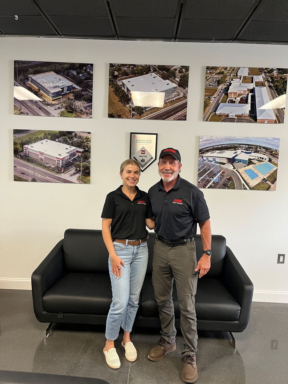 Two people standing in an office lobby in front of a black couch and wall photos.