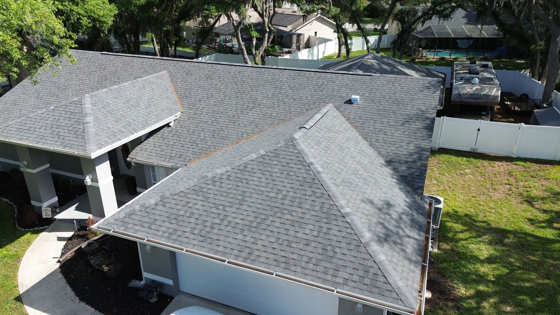 Aerial view of a gray shingle roof on a house with a fenced yard and driveway.