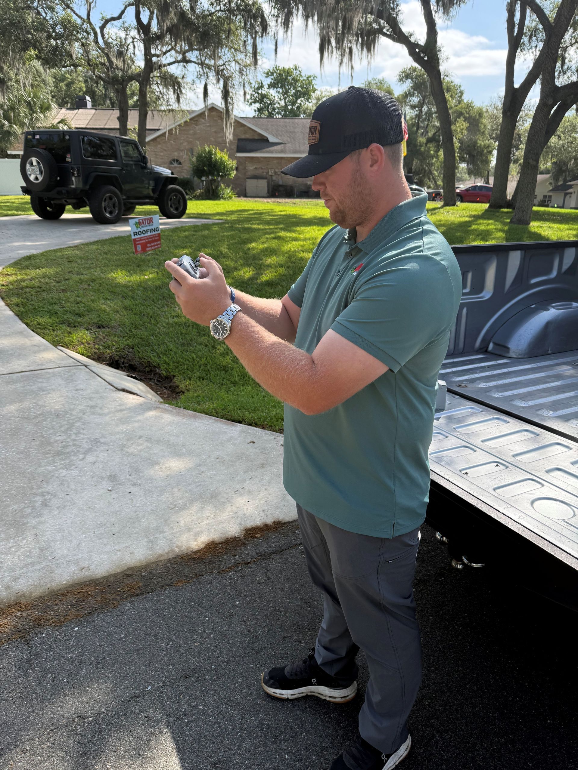 Man in a green shirt taking a photo beside a black truck in a sunny driveway.