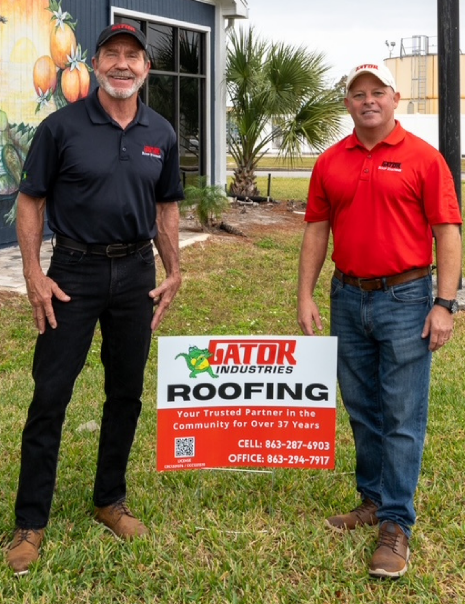 Two men in branded polo shirts stand in a grassy area, holding a sign for Gator Industries Roofing.