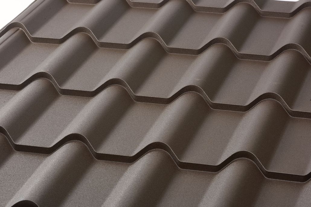 A close-up of dark brown, matte-textured metal roof tiles featuring a wavy, patterned design.