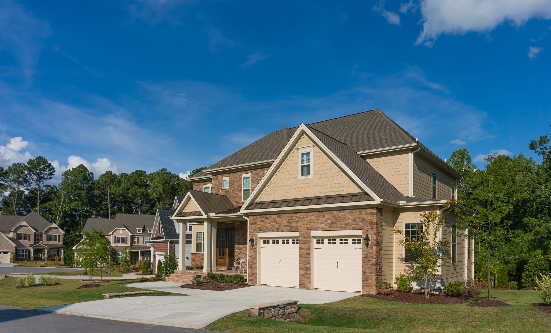 A two-story suburban house with brick and beige siding, a two-car garage, and a driveway under a clear blue sky.