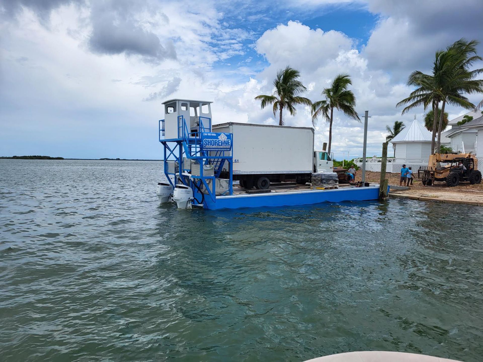 Blue ferry docked by palm trees on a choppy waterfront under cloudy skies