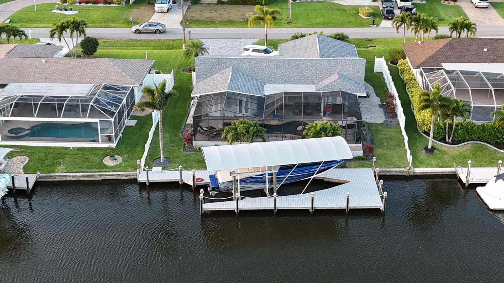 Aerial view of waterfront homes with screened patios, docks, and boat lifts along a canal.