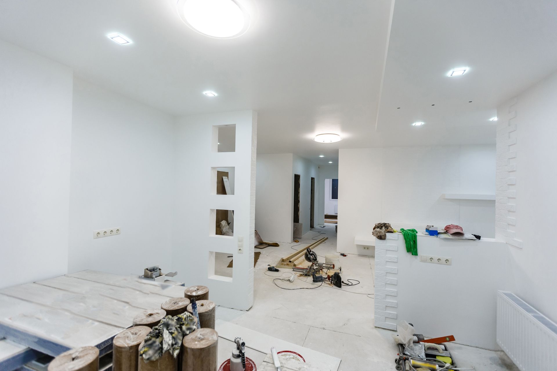Bright white unfinished room with construction tools, debris, and partially built walls and counters.
