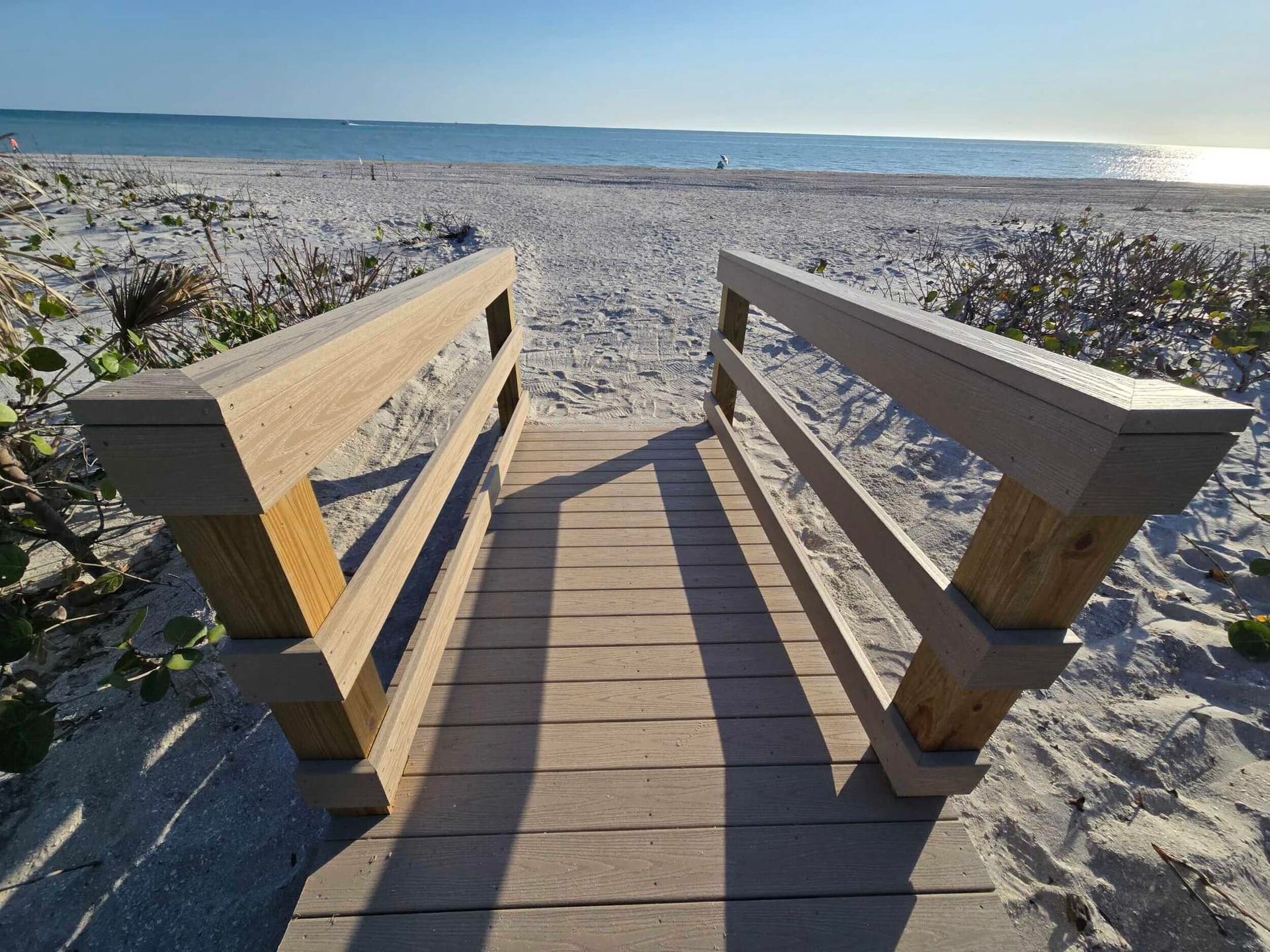Wooden boardwalk leading to a sunny beach with ocean horizon and sand dunes