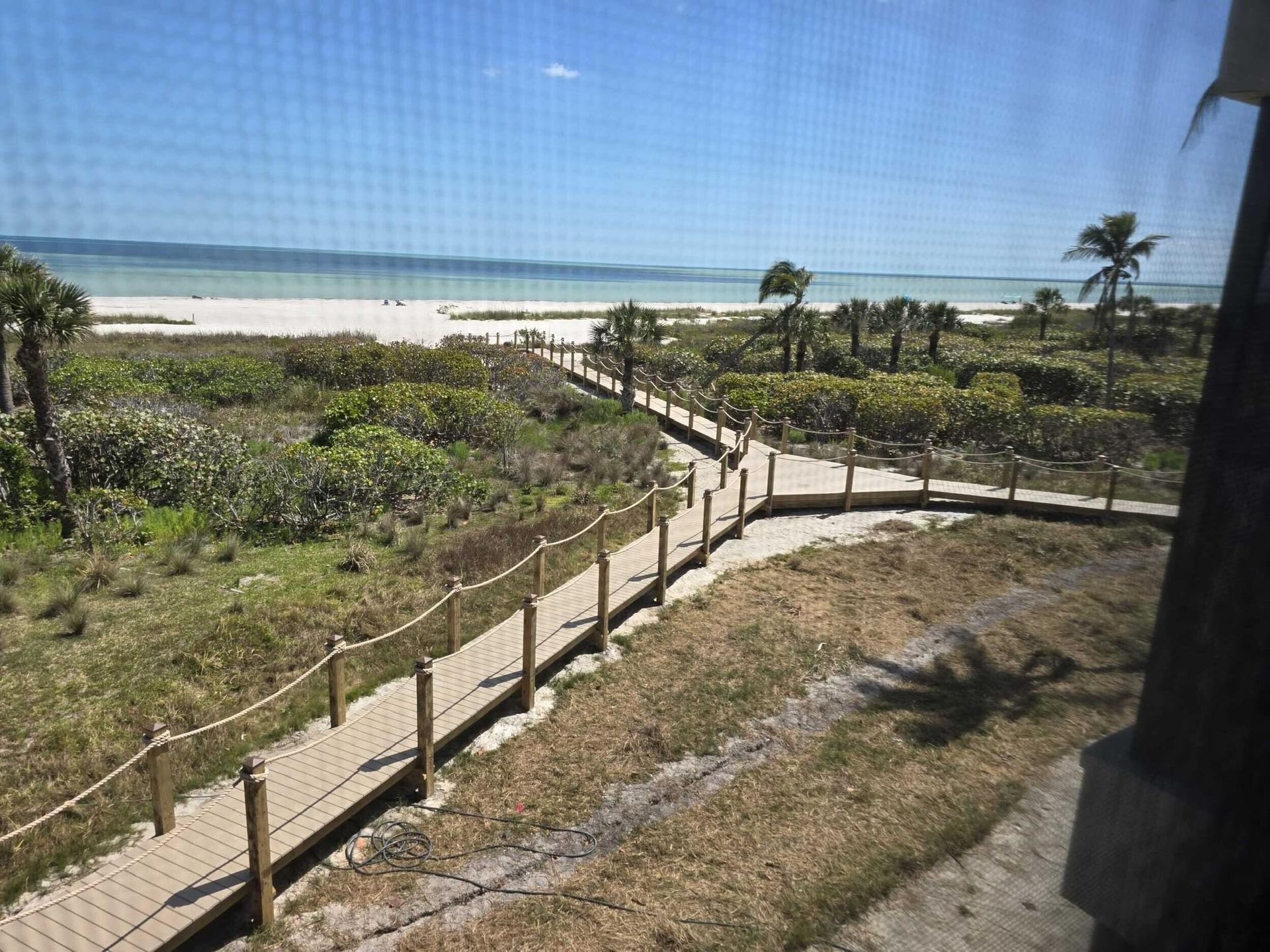 Beach walkway leading through dunes to a sandy shore and blue ocean under a clear sky