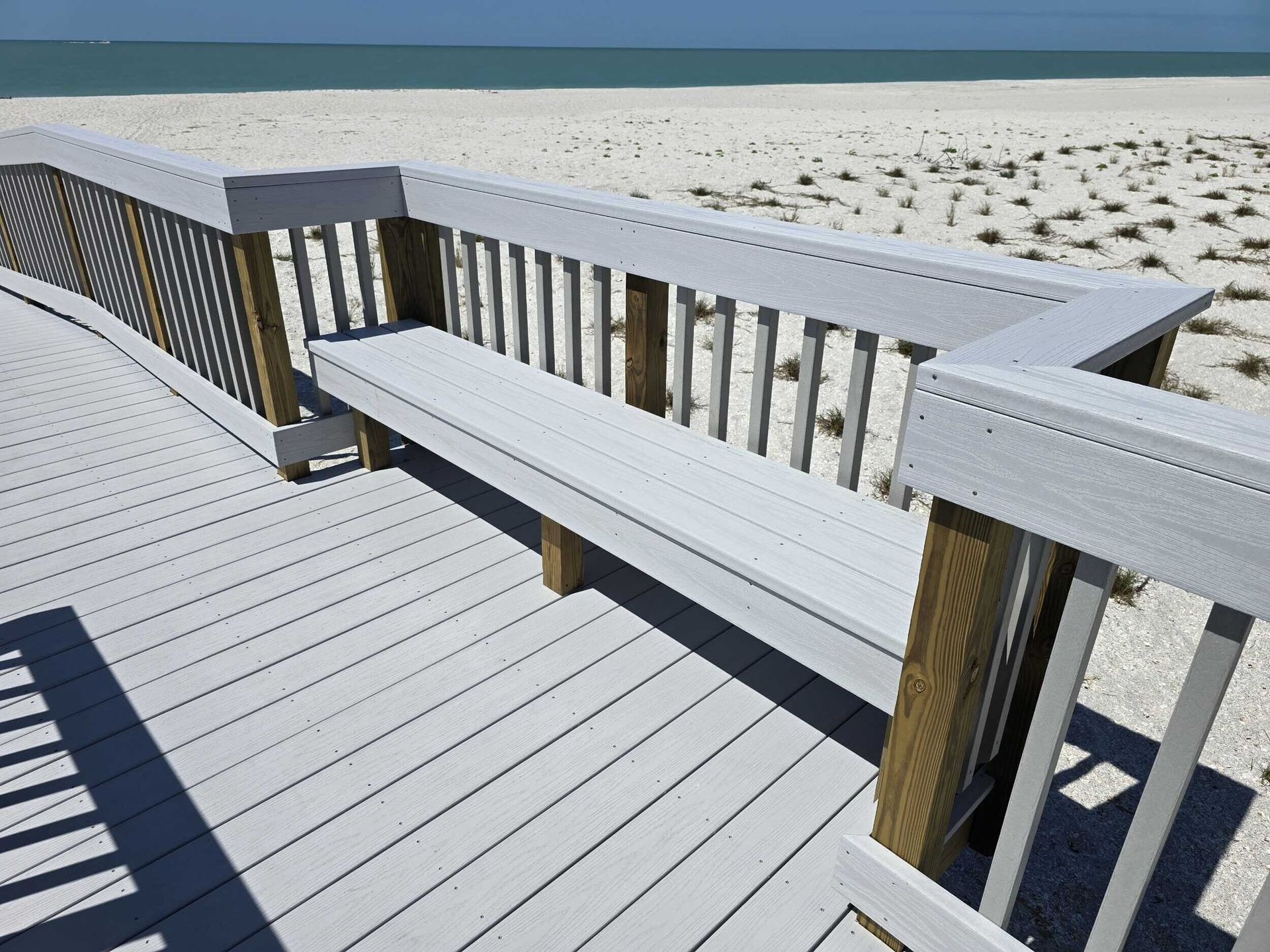 White boardwalk bench overlooking a sandy beach and ocean under a clear sky