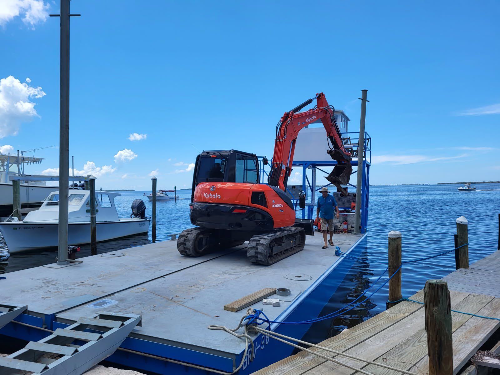 Orange excavator on a dock by the water, lifting equipment near boats on a sunny day