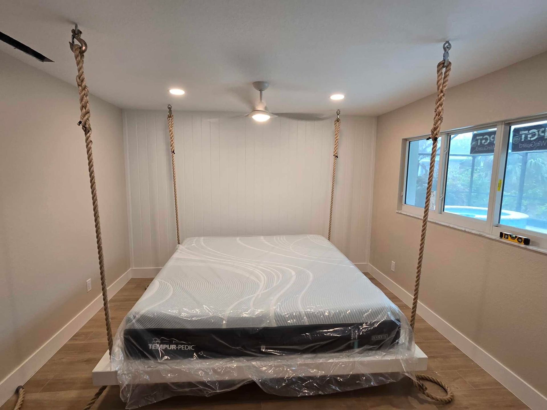 Unfinished bedroom with a bed wrapped in plastic, beige walls, and recessed lights