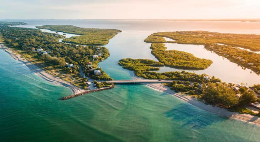 Aerial view of a tropical coastline with turquoise water, sandy beaches, and a narrow bridge to a small island