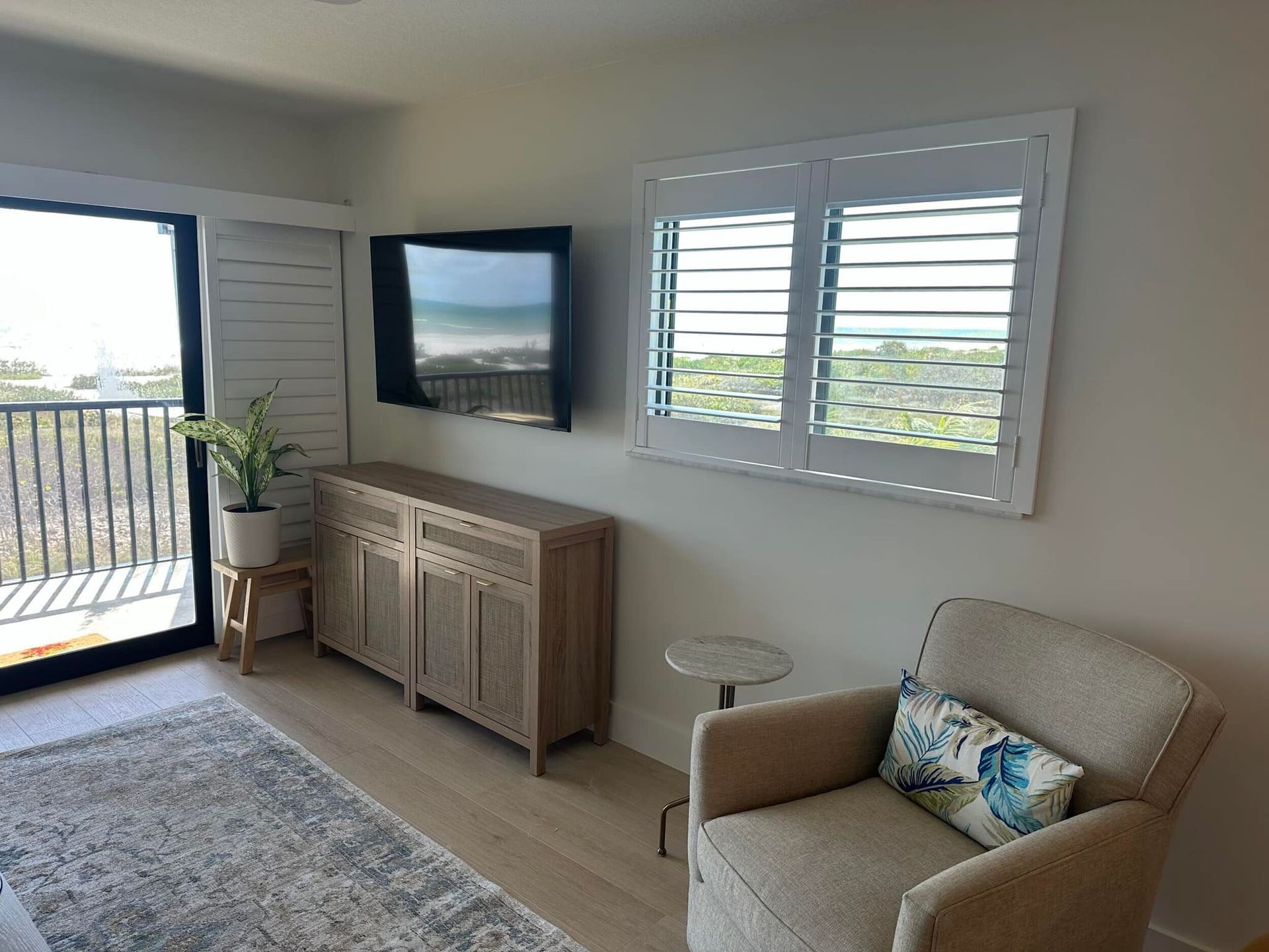 Bright coastal living room with TV, armchair, sideboard, and balcony doors