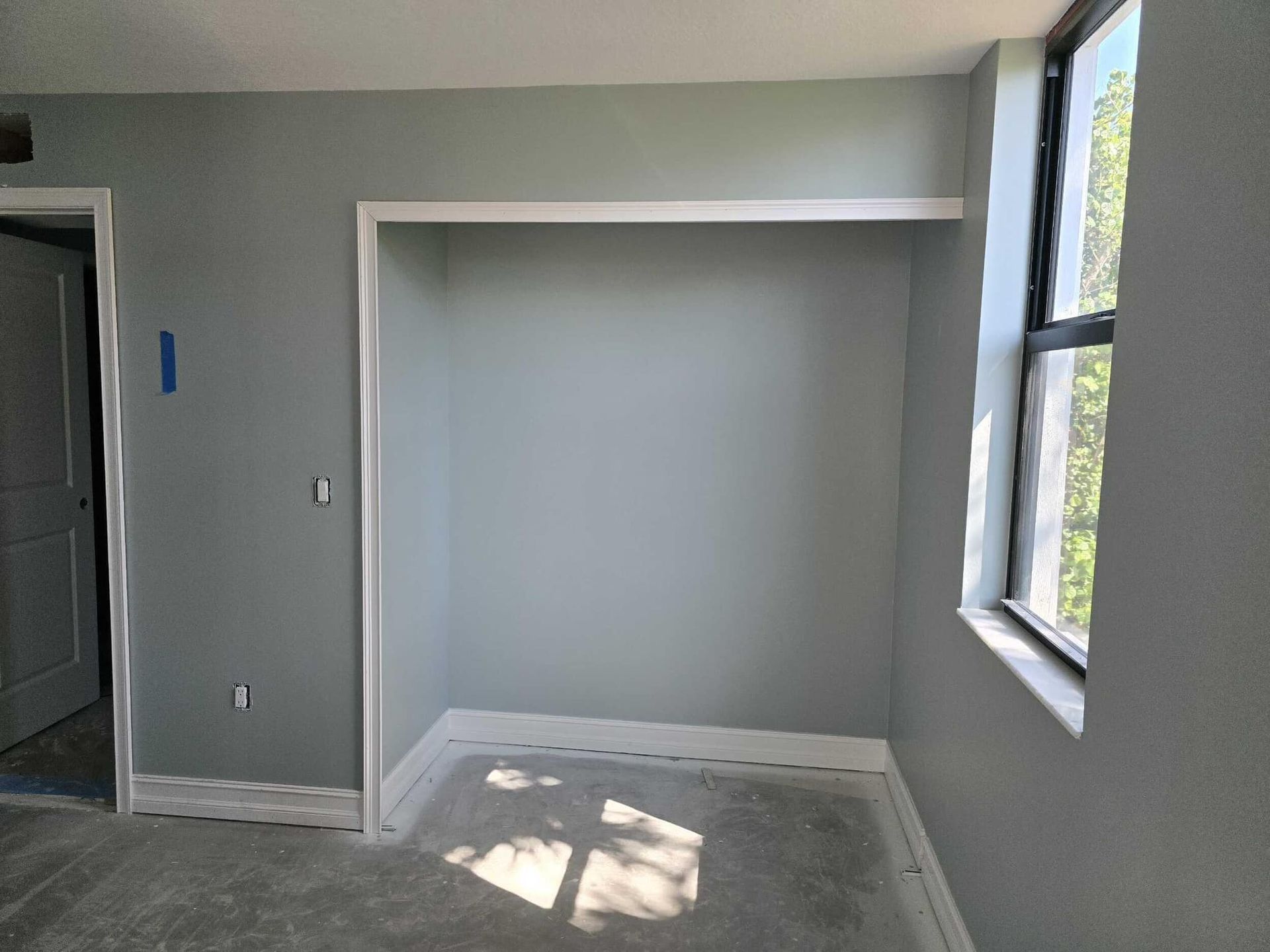 Empty gray room with white trim, window light, and a recessed wall alcove