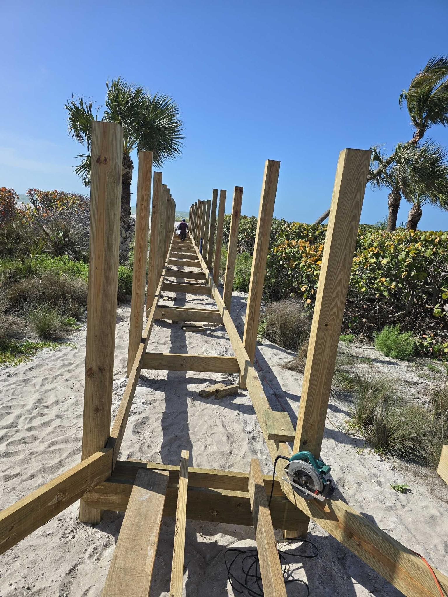 Wooden boardwalk under construction through sandy dunes, with posts and planks leading into the distance.