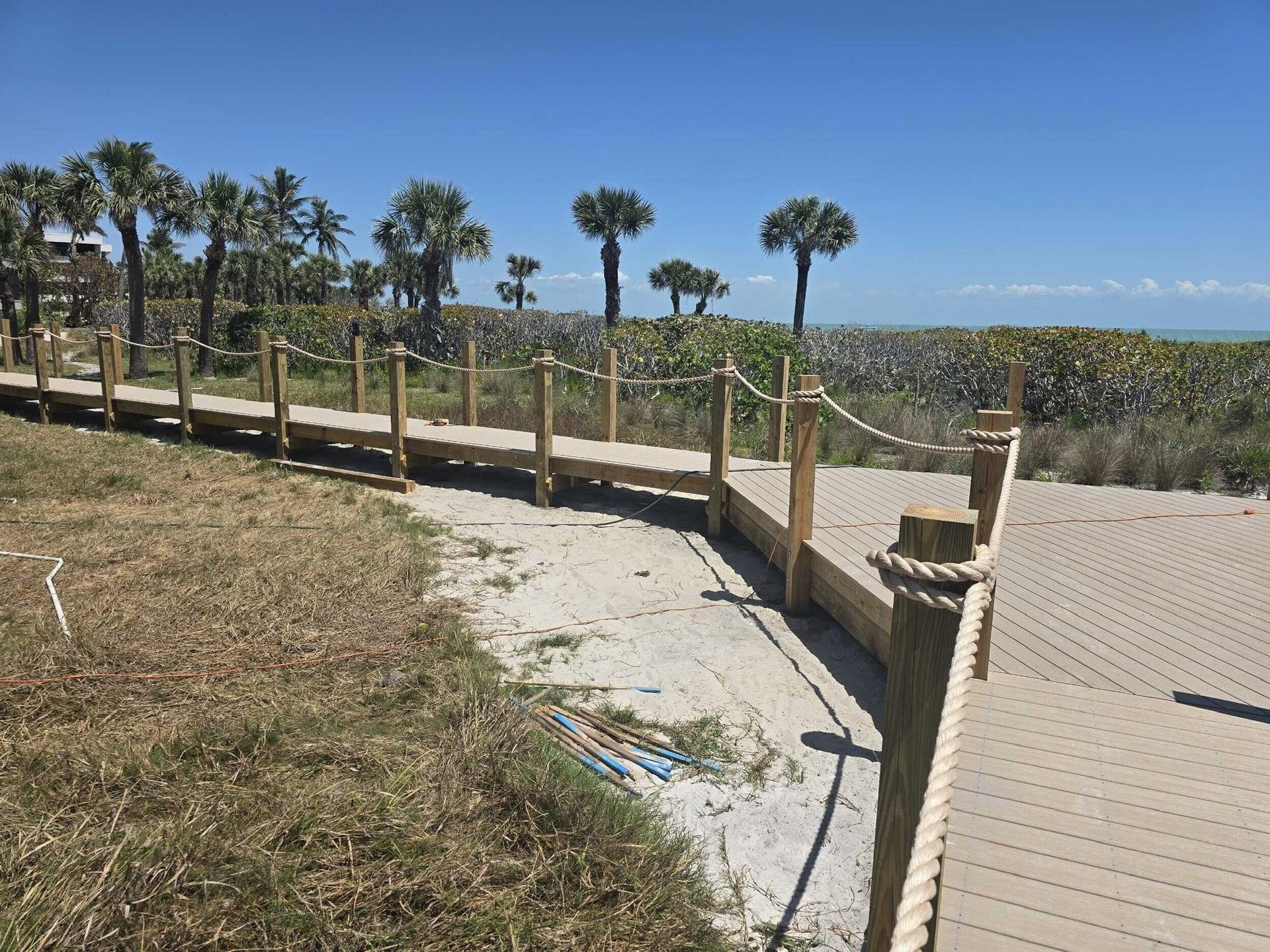 Wooden boardwalk overlooking a grassy coastal dune under a clear blue sky.