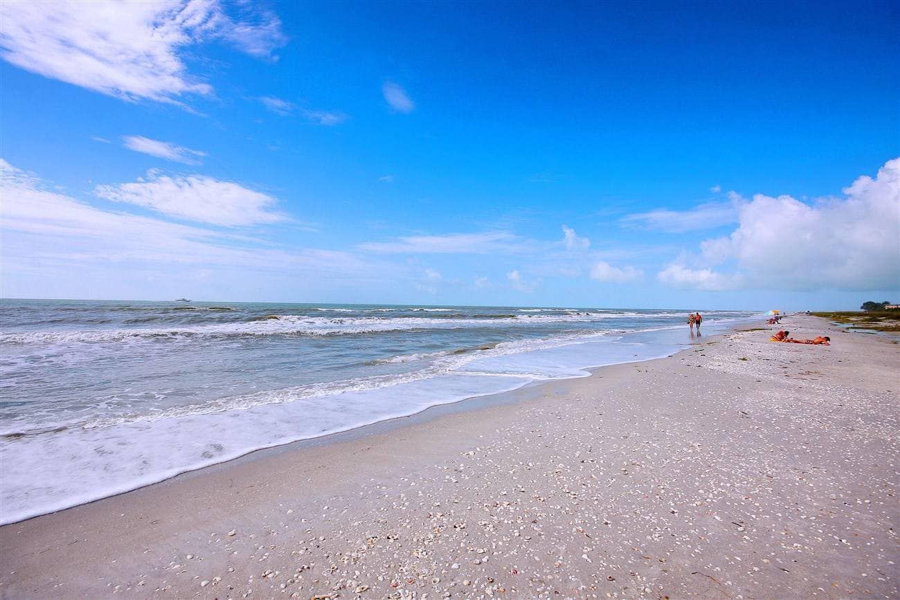 Sunny beach with gentle waves, blue sky, and a few people in the distance