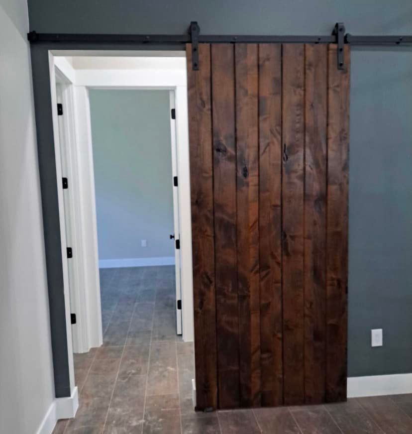 Interior hallway with a dark wood barn door on a gray wall, beside a white doorway.