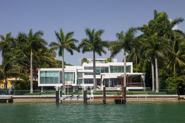 Modern waterfront villa with palm trees and a dock on calm water