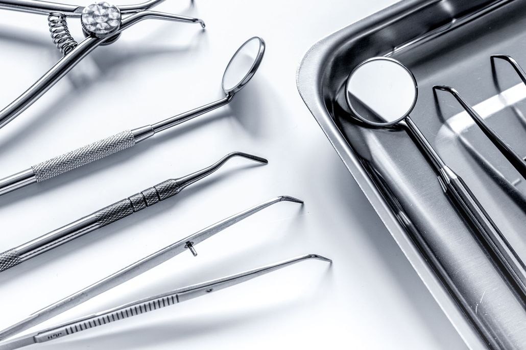 Assorted stainless steel dental instruments, including mouth mirrors and tweezers, arranged on a metallic tray.