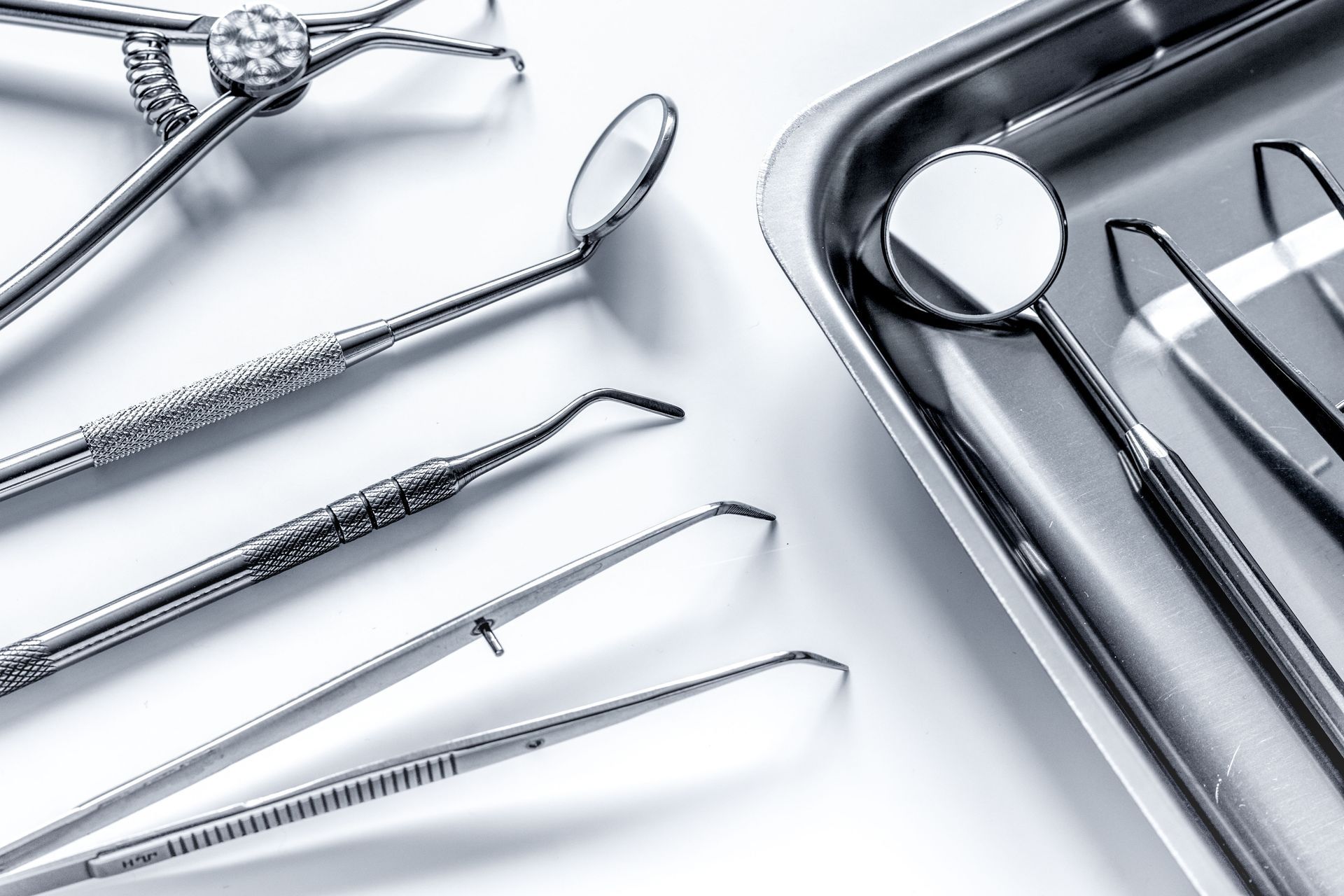 Assorted stainless steel dental instruments, including mouth mirrors and tweezers, arranged on a metallic tray.
