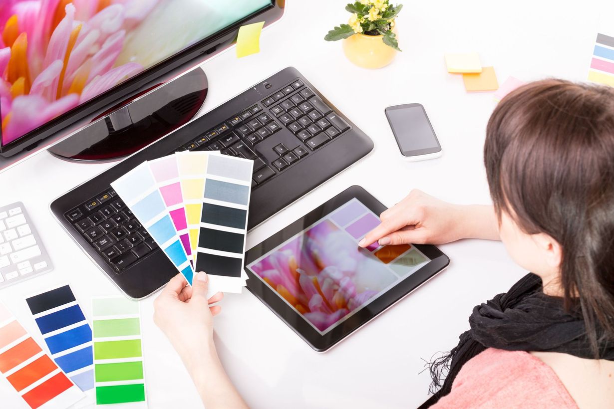 Woman working on digital art, using a tablet and color swatches on a white desk with a computer.