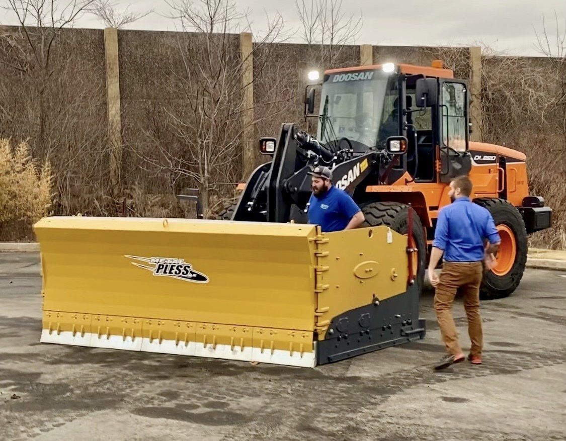 Two men are standing next to a large yellow snow plow