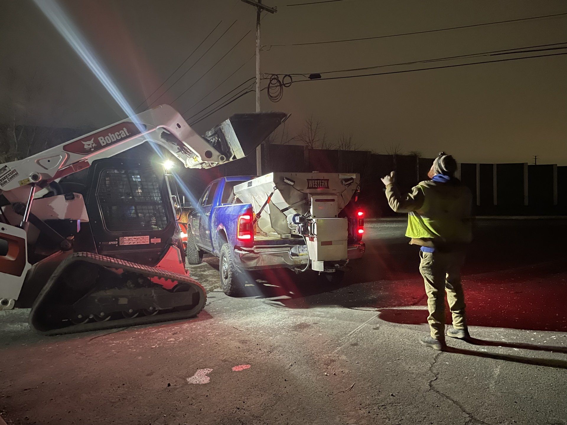 A man is standing in front of a bobcat tractor at night