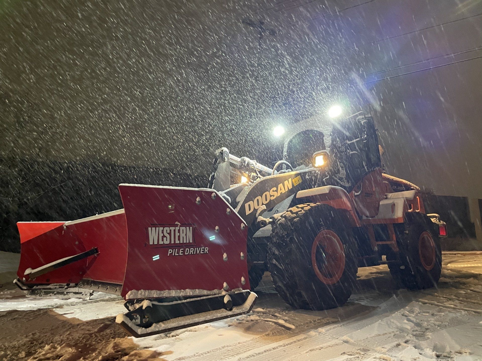 A snow plow is driving through the snow at night