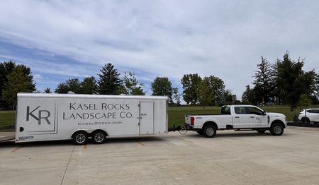 A truck is pulling a trailer that says kr landscape co. on it.