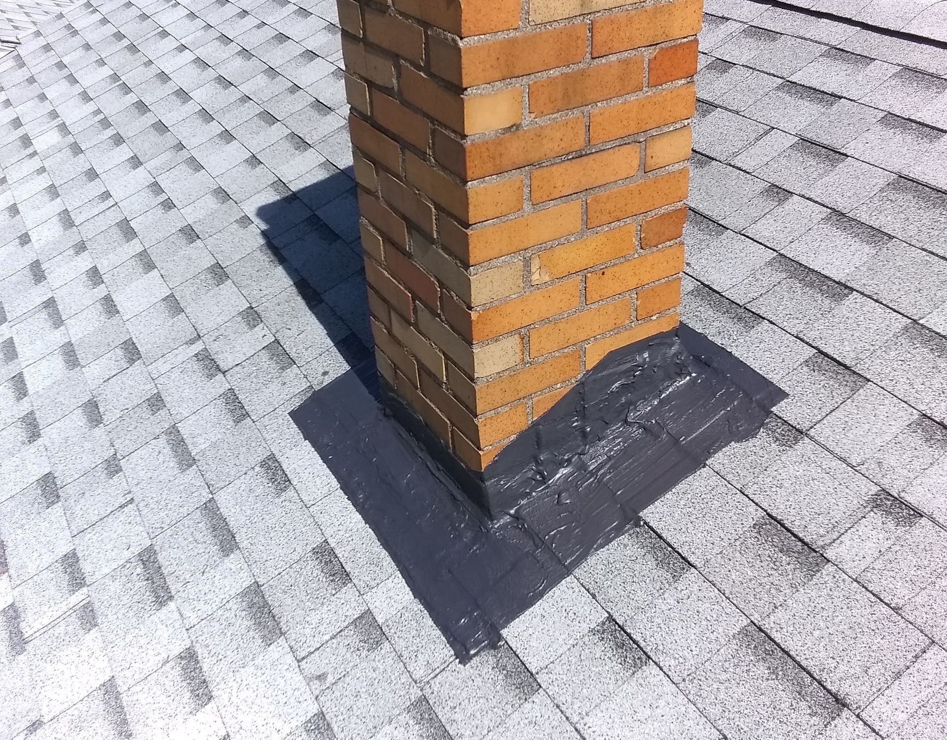 A brick chimney on top of a roof with shingles