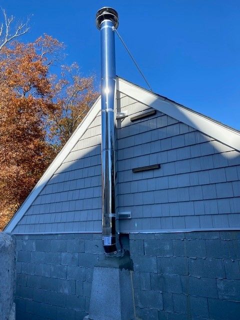 A stainless steel chimney is attached to the side of a house.