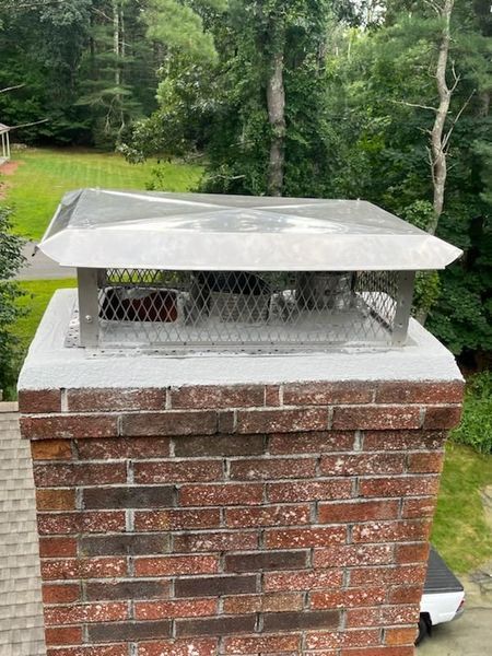 A brick chimney with a metal cover on top of it.
