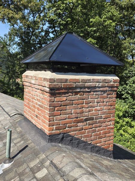 A brick chimney on top of a roof with trees in the background.