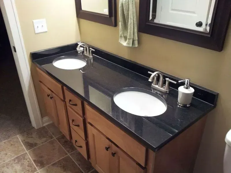 Bathroom vanity with black countertop, two sinks, and wood cabinets.