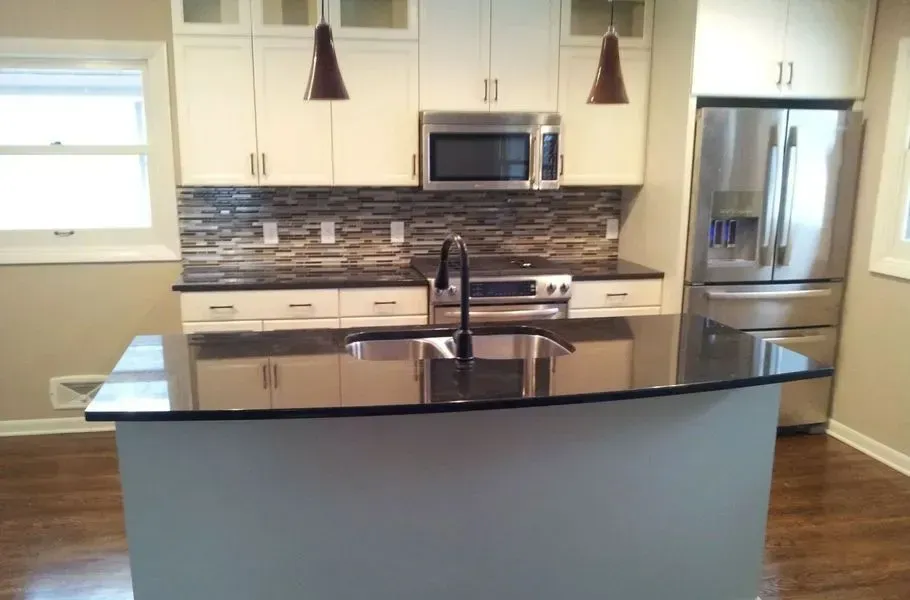 Modern kitchen with white cabinets, dark countertops, stainless steel appliances, and a central island.