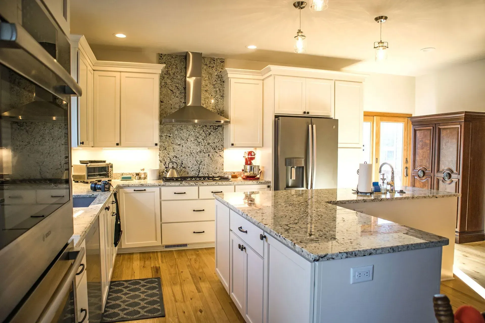 Bright white kitchen with granite countertops, stainless steel appliances, and wood flooring.