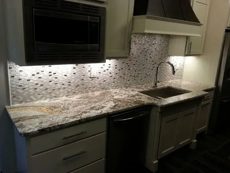 Kitchen with white cabinets, granite countertop, mosaic backsplash, microwave, and sink.