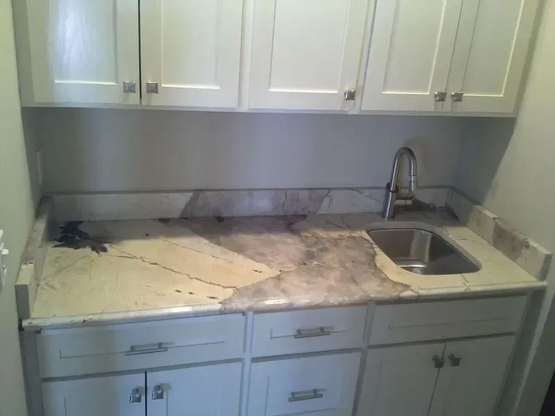 White cabinets with a granite countertop, sink, and faucet in a utility room.