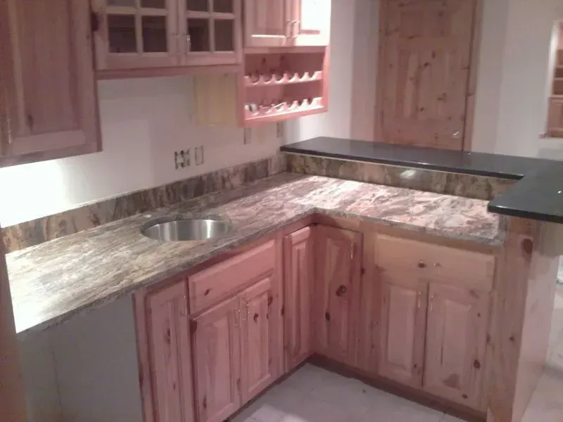 L-shaped home bar with light wood cabinets, granite countertops, a sink, and a wine rack.