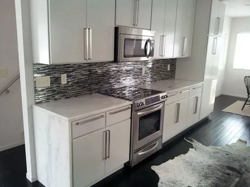 Modern kitchen with white cabinets, stainless steel appliances, and a mosaic backsplash.