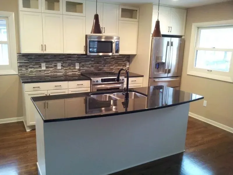Modern kitchen with white cabinets, dark countertops, island, stainless steel appliances, and brown pendant lights.