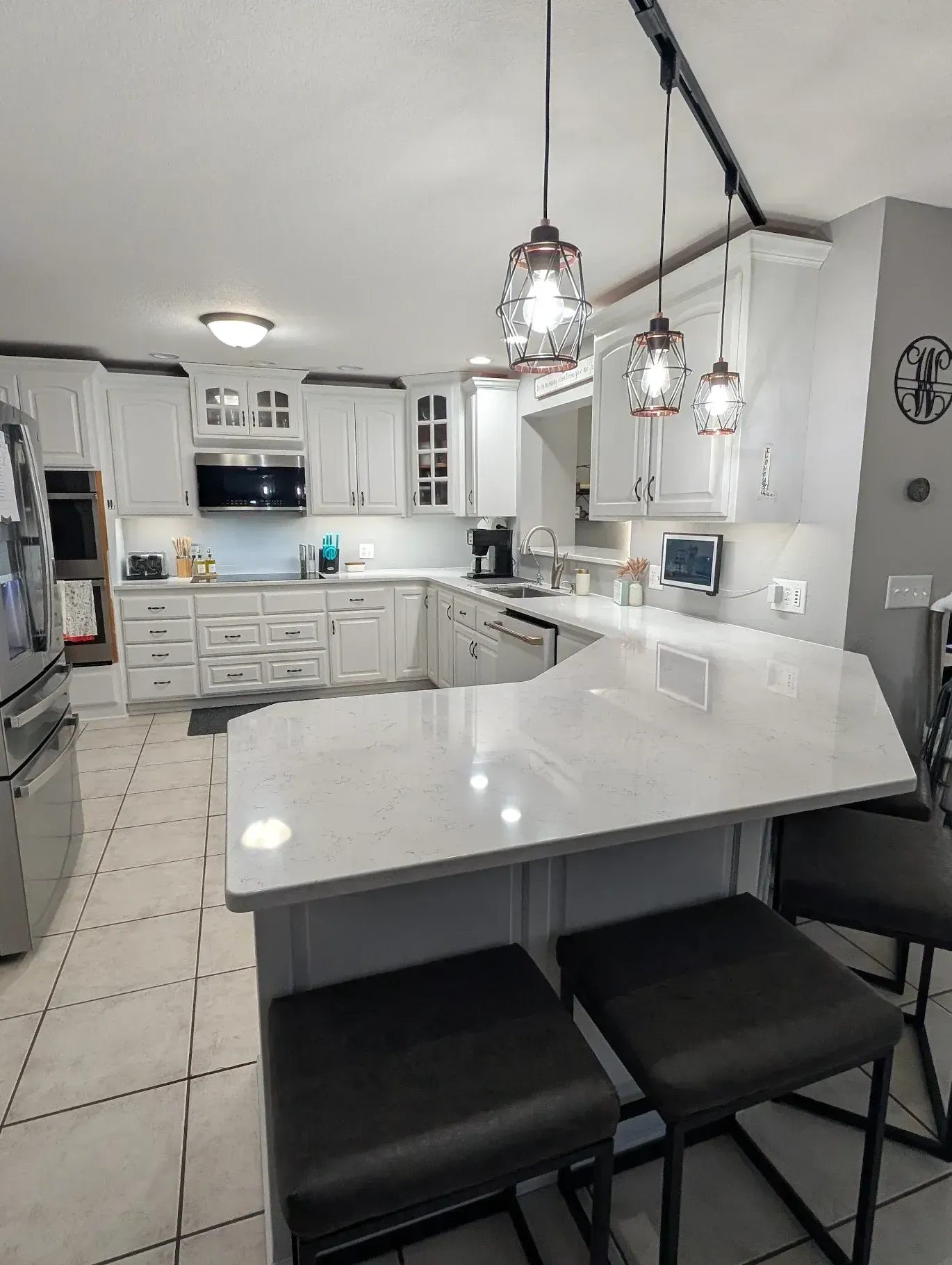 White kitchen with island and bar stools, overhead lights, cabinets, and appliances.