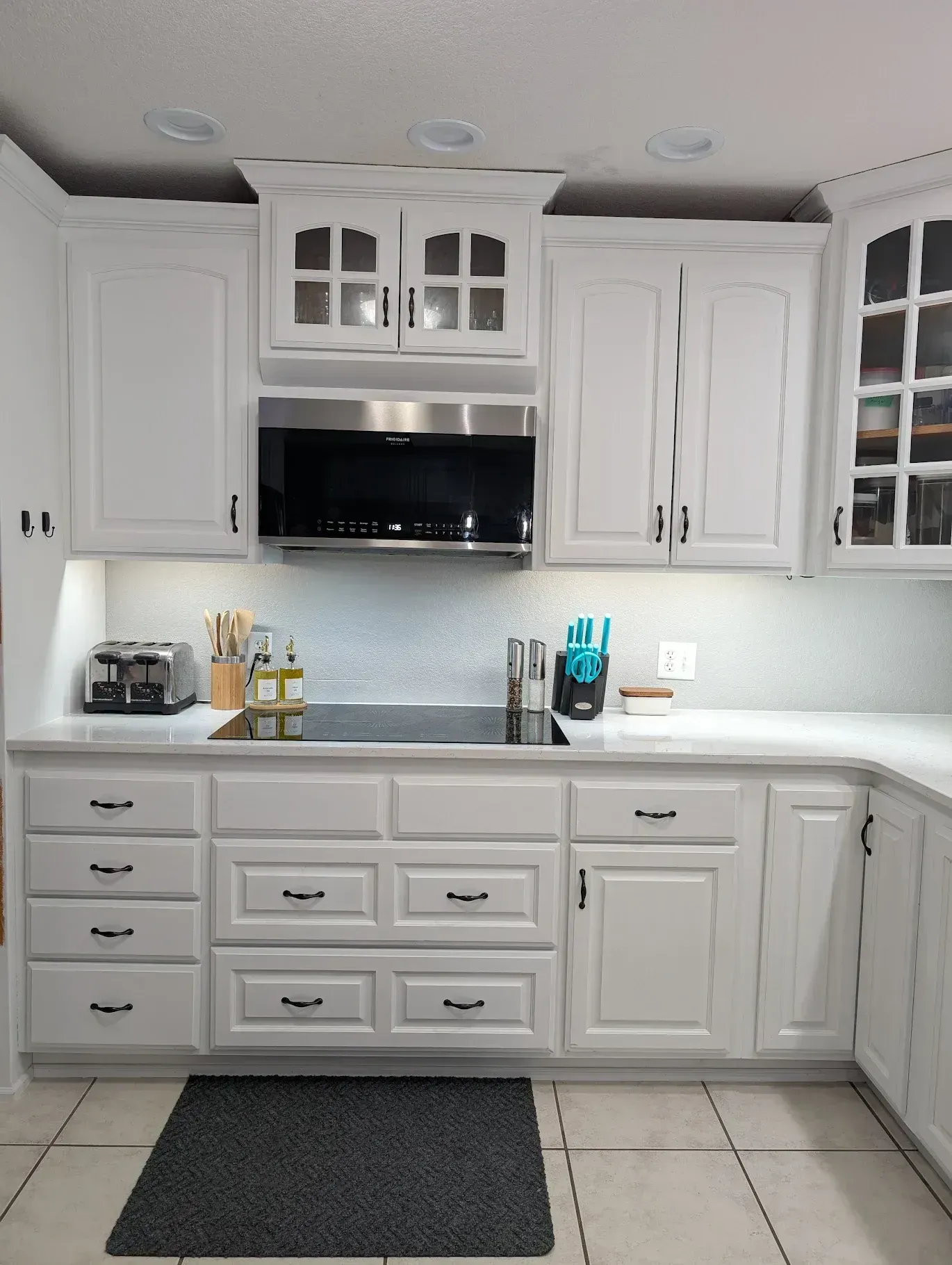 White kitchen cabinets, stainless steel microwave, black countertop, gray rug.