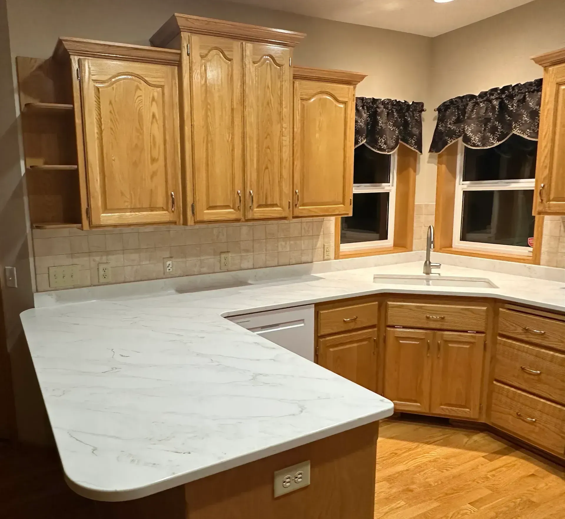 L-shaped kitchen with light wood cabinets, white countertops, and a window above the sink.