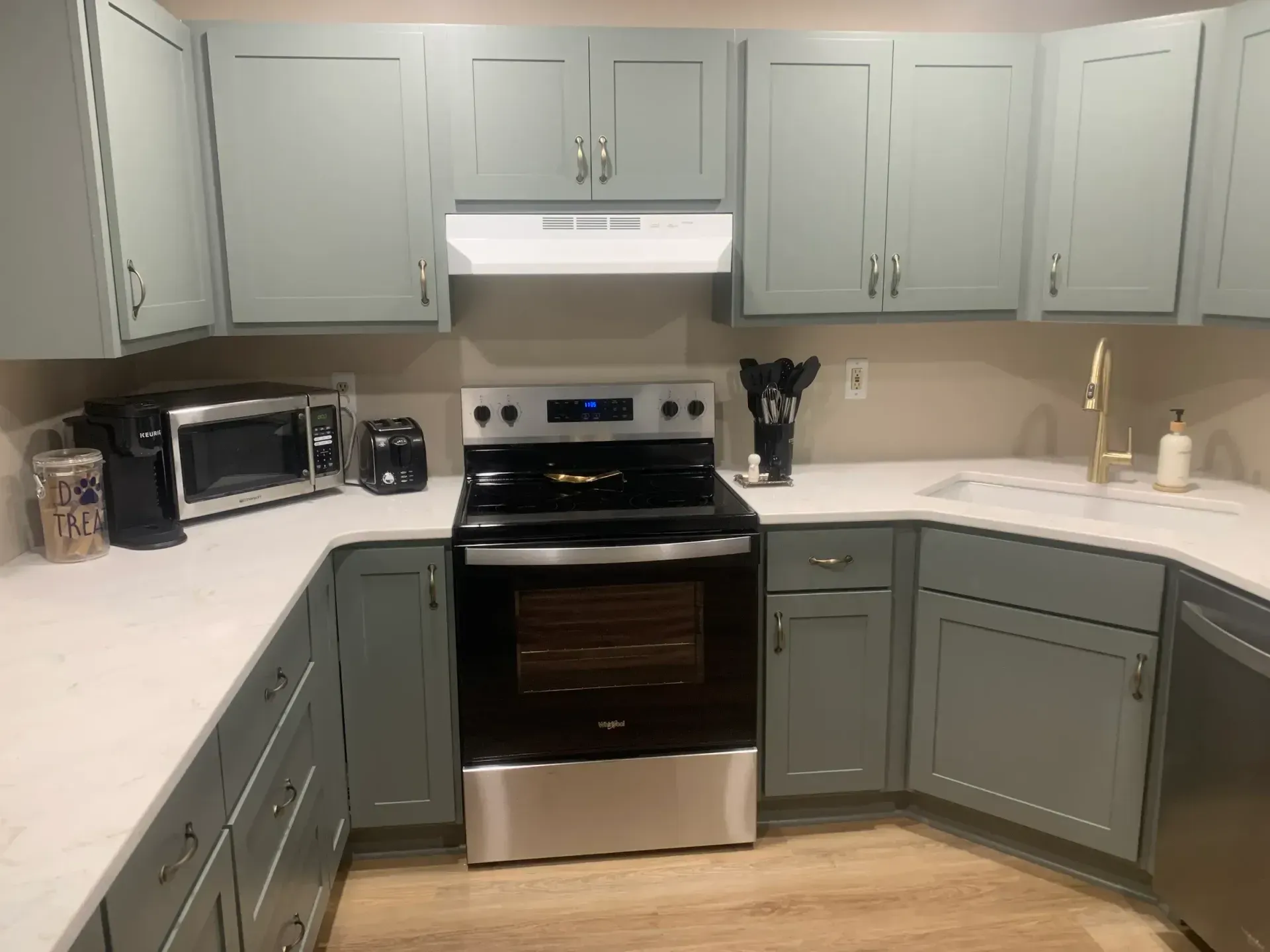 Kitchen with light green cabinets, white countertops, and a stainless steel oven.