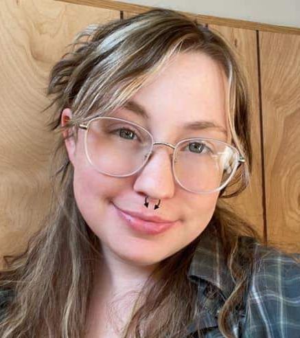 A woman wearing glasses and a nose ring is smiling for the camera.