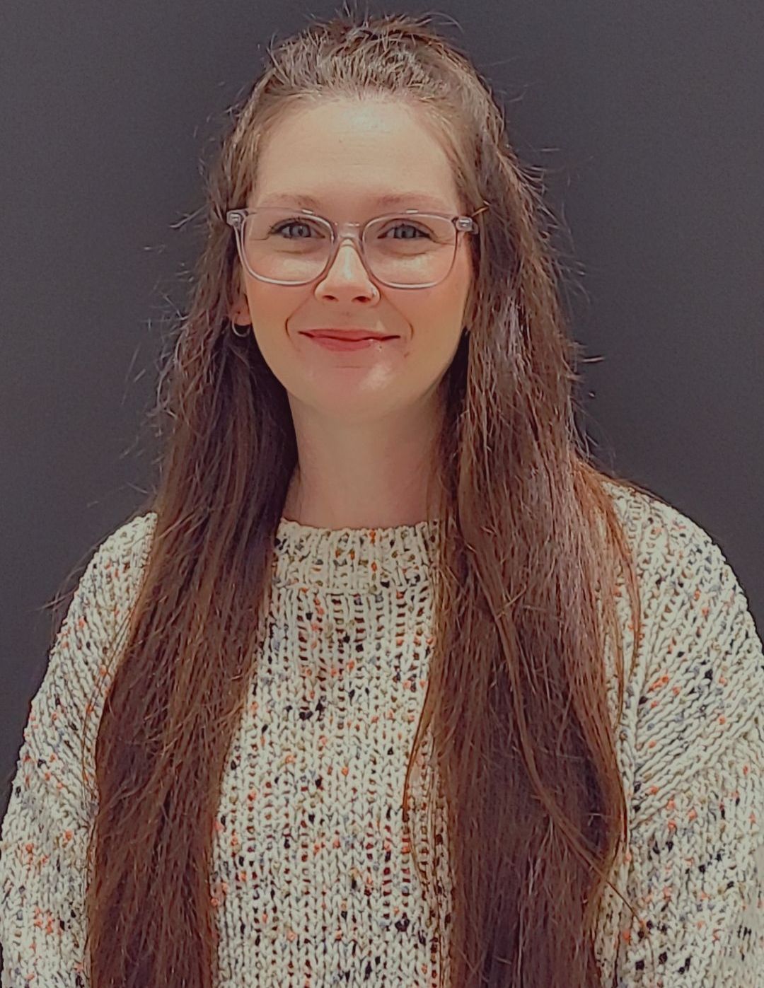 A woman with long hair and glasses is wearing a sweater.
